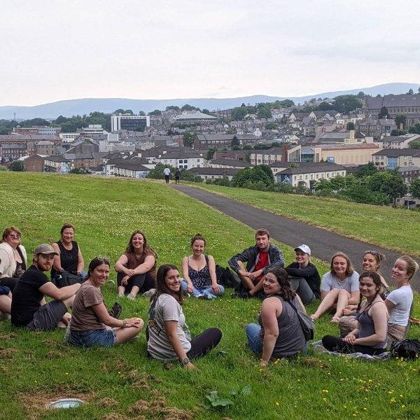 group of students seated in a circle on a hill with northern Ireland in the distance